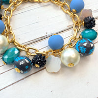 Lenora Dame jewelry. Blue and white beaded bracelet with assorted beads wire wrapped on a gold chain with lobster clasp. Black floral fimo beads, oval faceted glass beads, faux white pearls, blue rubberized beads, bumpy black beads and mother of pearl flower beads.