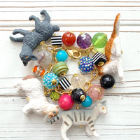 A charm bracelet with colorful beads, including red, green, blue, yellow, and purple. The bracelet also features small cat figurines in white, black, and gray. Gift for cat lovers. Lenora Dame jewelry.