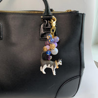 Cute bag charm for handbag with a mix of purple and gold beds on a gold chain and a black and white cat with chain collar hanging at the bottom. Lenora Dame bag charm. Beaded purse charm.