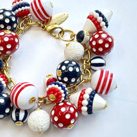 Patriotic charm bracelet with a mix of red, white and blue beads. Gold bracelet chain with lobster clasp and a Lenora Dame hang tag features blue and red round polka dot beads, and red, white and blue striped beads. Lenora Dame bracelet made in the USA.