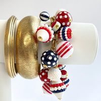 Patriotic charm bracelet with a mix of red, white and blue beads. Gold bracelet chain with lobster clasp and a Lenora Dame hang tag features blue and red round polka dot beads, and red, white and blue striped beads. Lenora Dame bracelet made in the USA.