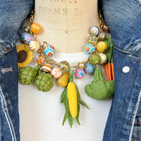 Colorful vegetable necklace for women with colorful beads and vegetable charms that include corn, artichokes, broccoli, carrots, and a sunflower. Wacky necklace for women with vegetable charms shown on a dress form wearing a white t-shirt and denim jacket. Lenora Dame necklace made in the USA.