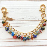 Assorted color and shaped floral glass millefiori glass beads dangling from a gold purse bag chain. Floral lampwork beads on a gold chain. Lenora Dame bag chain.