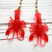 Red lobster dangle earrings for women with soft resin lobsters hanging by the tail from a chain made with 4 linked pearls, hung on French ear wires. Cute lobster earrings. Lenora Dame jewelry.
