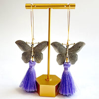 Butterfly dangle earrings with silver metal butterflies, hanging from long oval gold hoop ear wires. Light purple silky tassels hang from the bottom of the butterfly earrings. Lenora Dame Jewelry made in the USA.