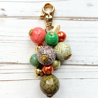 Beaded bag charm with large round beads in a mix of designs in a cluster under a gold trigger clasp. Three beads are wood decoupaged in modern animal prints such as snake print and zebra print. The other beads are gold, rust, green and pink. Lenora Dame bag charm.