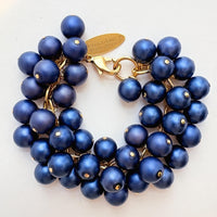 A gold chain bracelet with multiple strands of matte navy blue faux pearls. The bracelet has a small tag that reads 'Lenora Dame' and 'Made in the USA.'