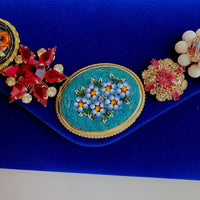 Miniature floral mosaic brooch, and other rhinestone and pearl pieces on a blue velvet clutch purse.