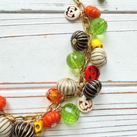 Lenora Dame necklace with a gold chain filled with orange and white jack o lantern beads, orange pumpkins, yellow sugar skull beads, black pumpkins, and green beads. Cute necklace for fall.