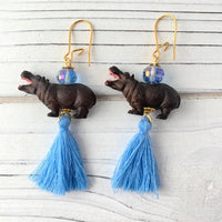 Hippo earrings with miniature brown hippopotamus, topped with a small faceted light blue bead, and blue thread tassels hanging below. Earrings have gold ear wires.