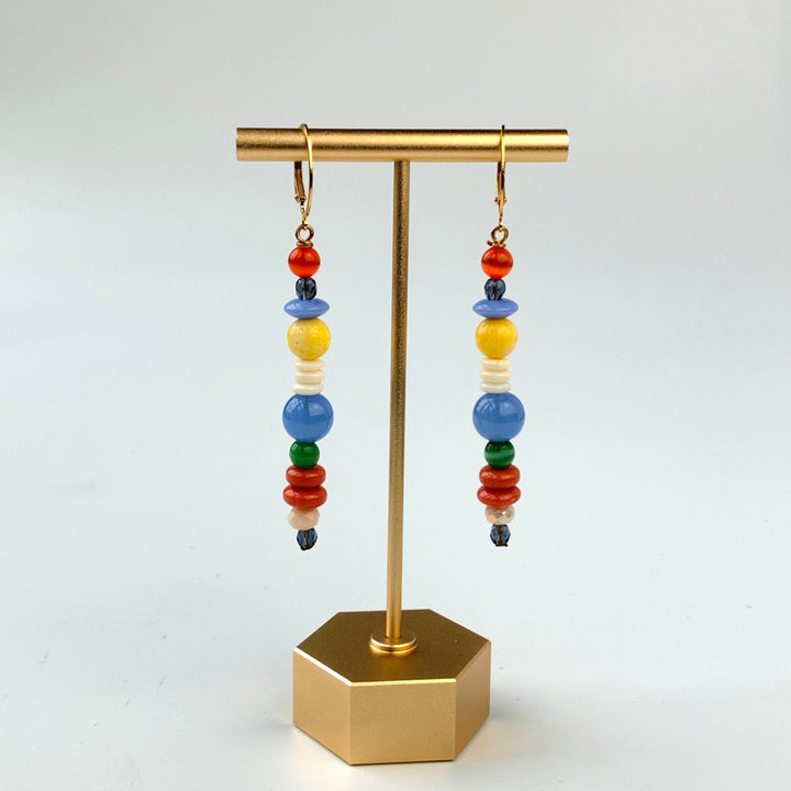 A pair of long skinny earrings with different shaped red, blue, white, and yellow beads. Lenora Dame earrings.