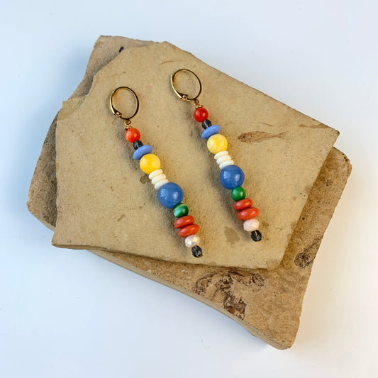 A pair of long skinny earrings with different shaped red, blue, white, and yellow beads. Lenora Dame earrings.