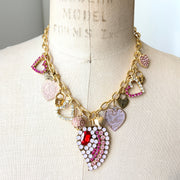 Gold chain necklace with a mix of dangling heart shaped charms and a bigger center heart charm embellished with pink rhinestones.