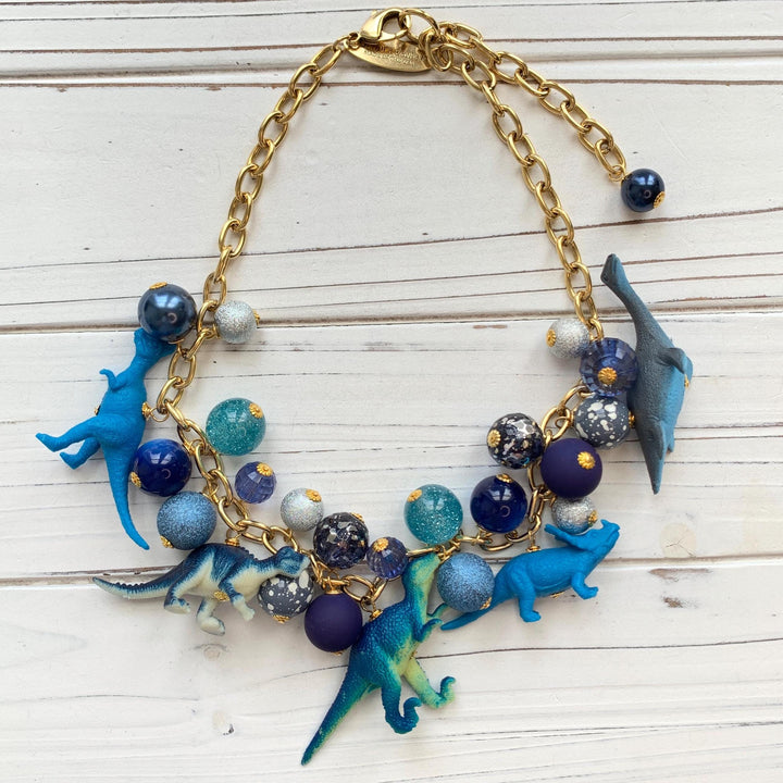 Blue necklace with miniature dinosaur charms on a gold chain. Whimsical dinosaur necklace for women.