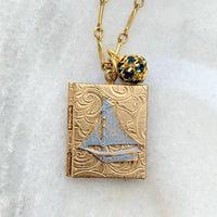 Gold locket necklace with brass sailboat metal stamping detail hung on a gold chain. Locket necklace for women.