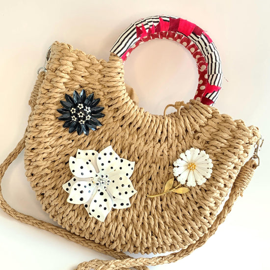 Cute straw bag for summer detailed with large metal flower brooches and contrast top handle wrapped in red and black fabric. Small woven handbag for casual summer style.