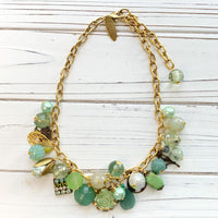 Gold chain charm necklace filled with assorted green beads and charms hanging from a gold cable chain. Lenora Dame necklace. Green statement necklace.