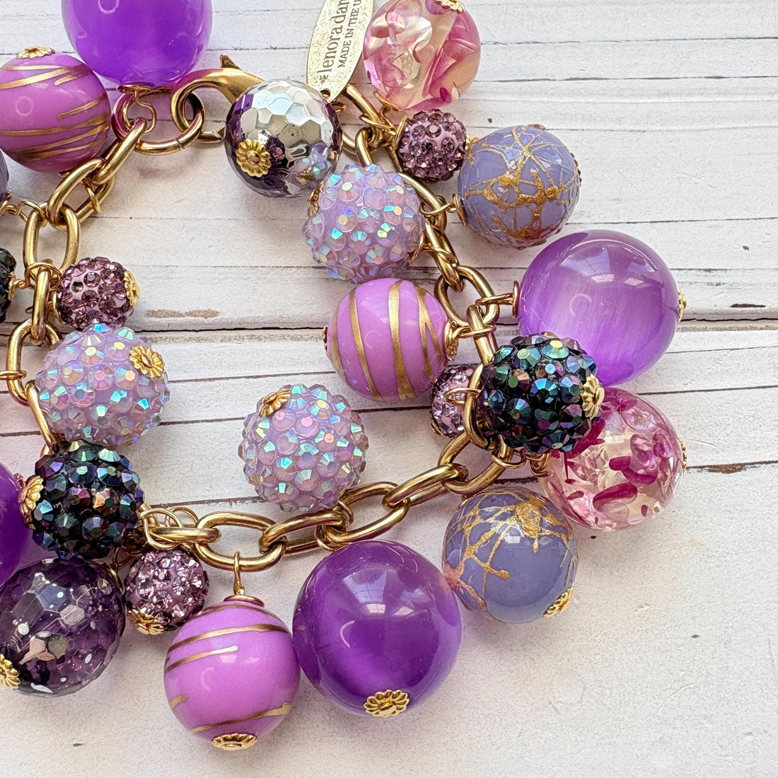 Beaded purple bracelet with assorted mix of purple beads on a gold chain and a Lenora Dame hangtag. Purple chunky bracelet. Lenora Dame jewelry made in the USA.