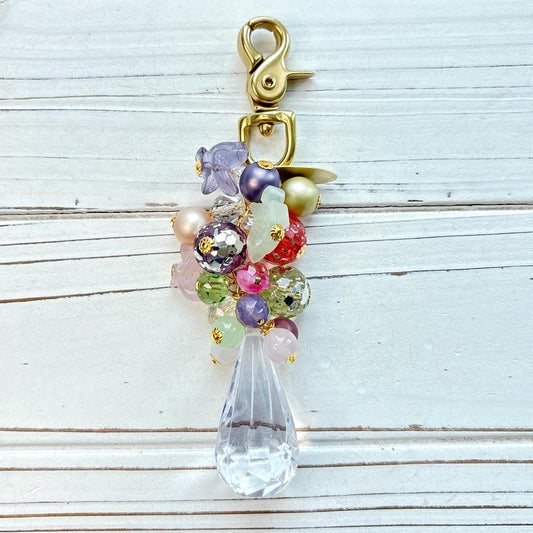 Pastel beaded bag charm with gold trigger clasp. Assorted pastel beads and glass birds hang above a long teardrop shaped faceted Lucite crystal. Lenora Dame bag charm.