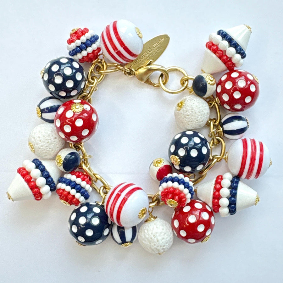 Patriotic charm bracelet with a mix of red, white and blue beads. Gold bracelet chain with lobster clasp and a Lenora Dame hang tag features blue and red round polka dot beads, and red, white and blue striped beads. Lenora Dame bracelet made in the USA.