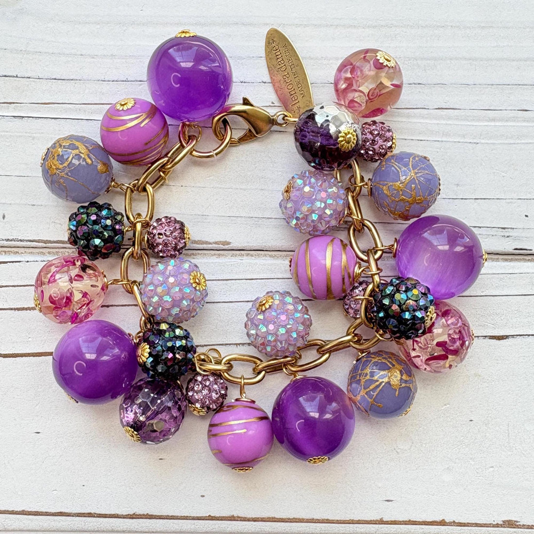 Beaded purple bracelet with assorted mix of purple beads on a gold chain and a Lenora Dame hangtag. Purple chunky bracelet. Lenora Dame jewelry made in the USA.