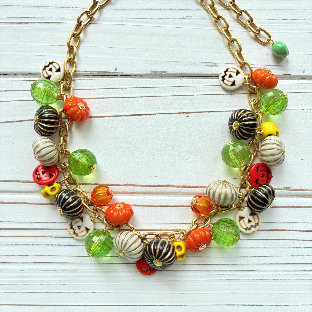 Lenora Dame necklace with a gold chain filled with orange and white jack o lantern beads, orange pumpkins, yellow sugar skull beads, black pumpkins, and green beads. Cute necklace for fall.